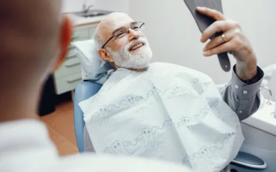 Patient smiling in dental chair, holding mirror, showcasing satisfaction with dental care at Hastings Dental Studio.