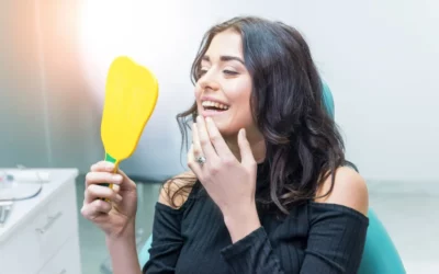 Smiling woman holding a mirror in a dental office, showcasing her enhanced smile after cosmetic bonding treatment.