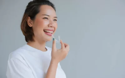 Woman smiling while holding a mouthguard, illustrating the benefits of mouthguards for relieving TMD symptoms in dental care.
